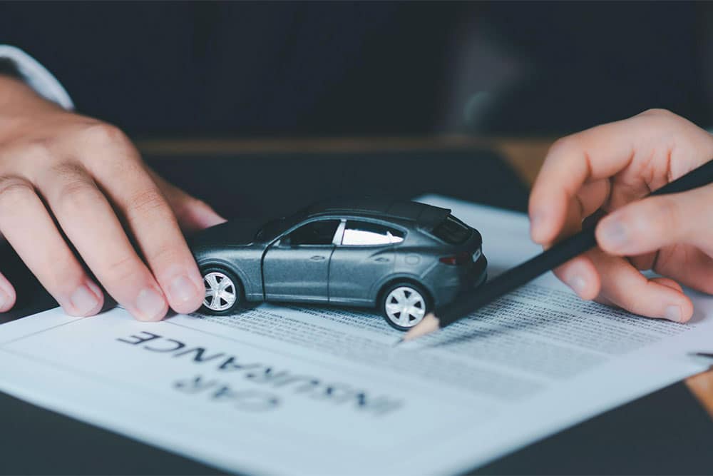 Hands holding a miniature car model on top of an insurance contract document, representing auto insurance coverage and policy signing