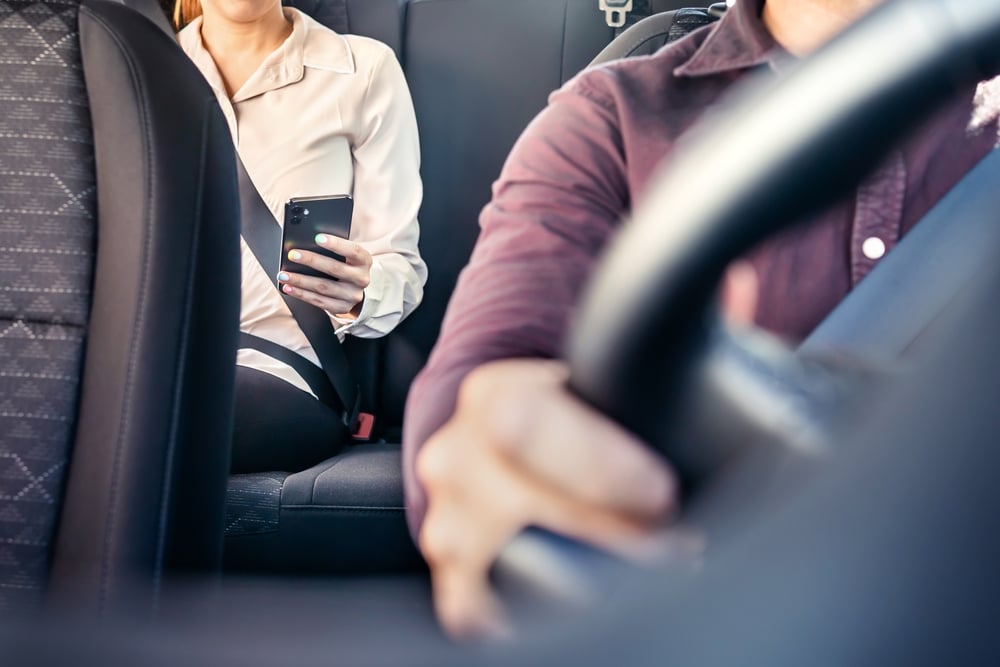 Passenger using a phone in the back seat of a rideshare vehicle, illustrating risks tied to Rideshare Accidents on Long Island.