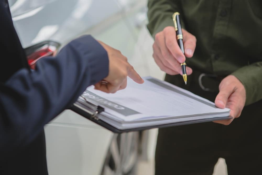 Person signing paperwork next to a damaged car, representing claims after Rideshare Accidents on Long Island.