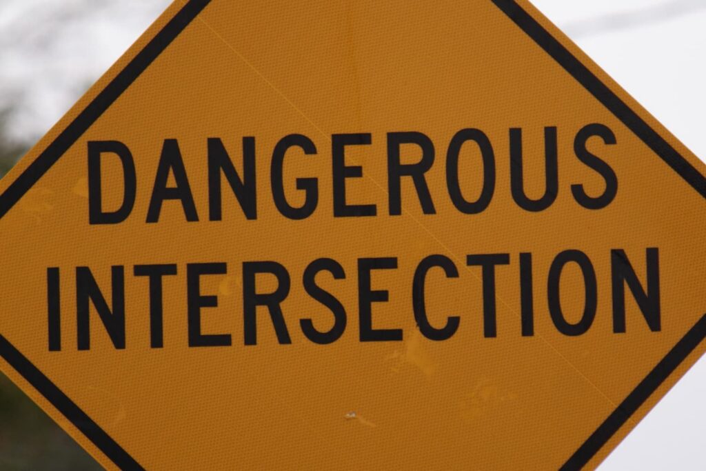 Yellow diamond warning sign reading “Dangerous Intersection” indicating high-risk roadway crossing