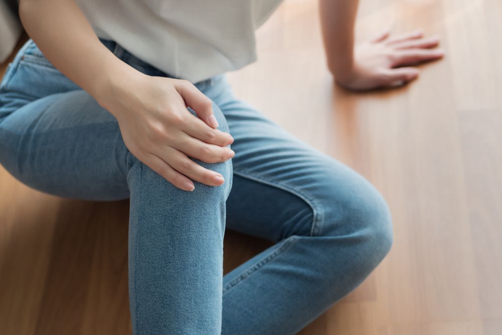Person sitting on the floor holding their knee in pain after an injury or fall.