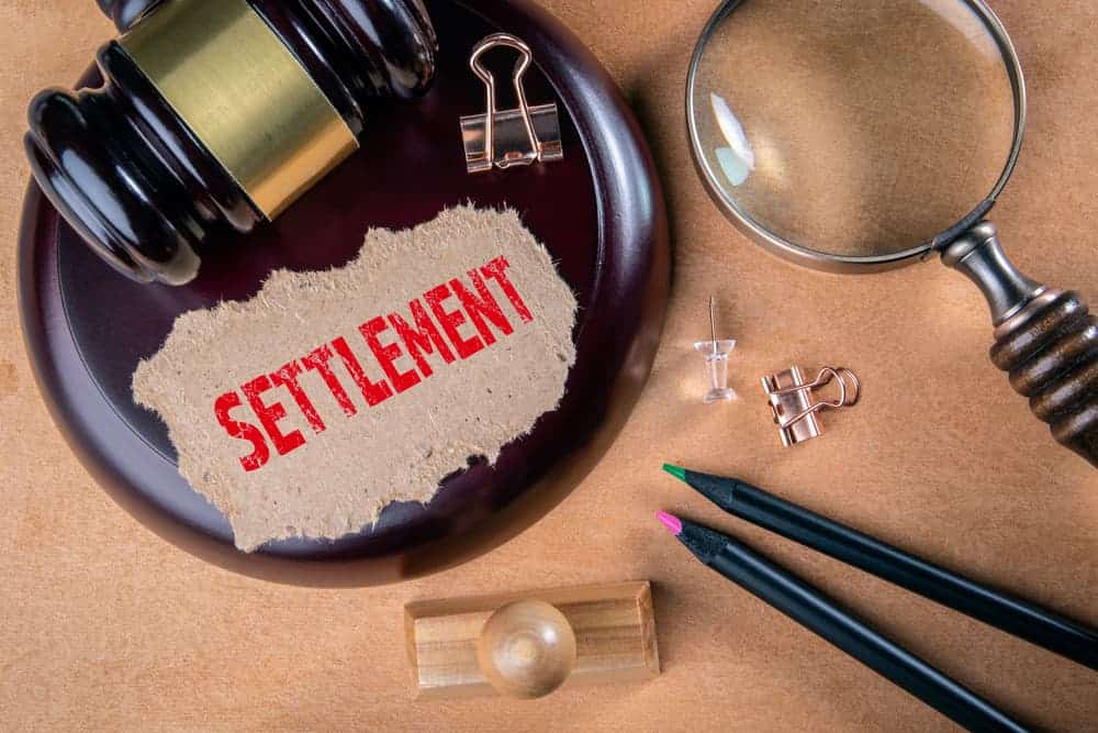 Legal settlement concept with judge’s gavel, magnifying glass, and settlement document on desk.