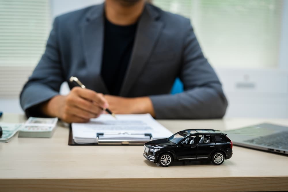 Car insurance agent reviewing paperwork with vehicle model on desk during auto insurance claim process.