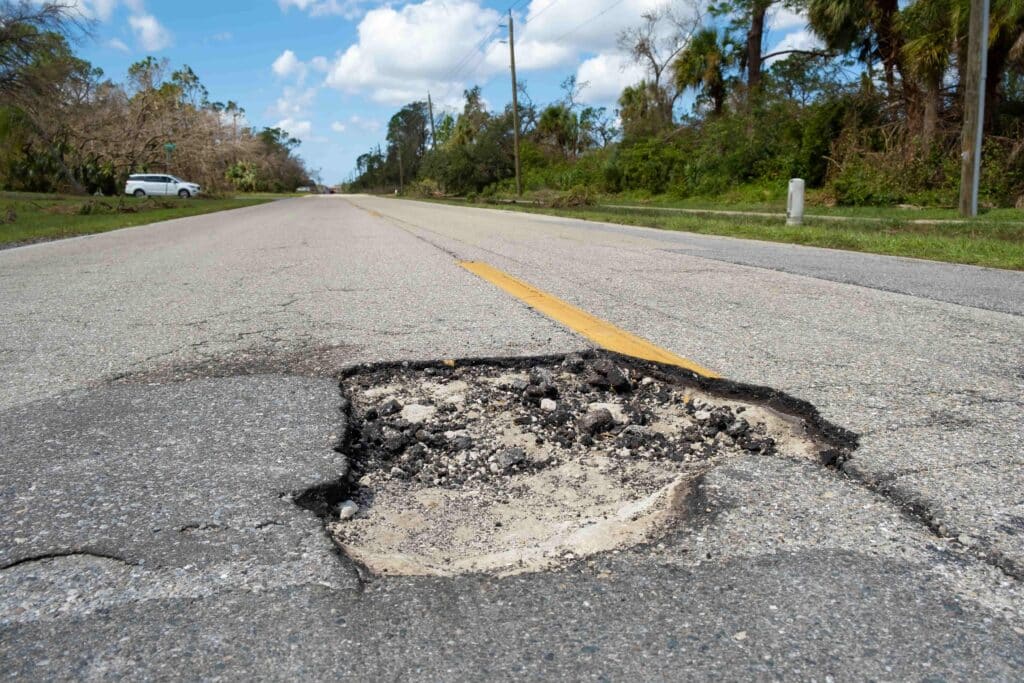 Large pothole in the middle of a roadway creating a dangerous driving hazard and potential accident risk. Large pothole in the middle of a roadway creating a dangerous driving hazard and potential accident risk.