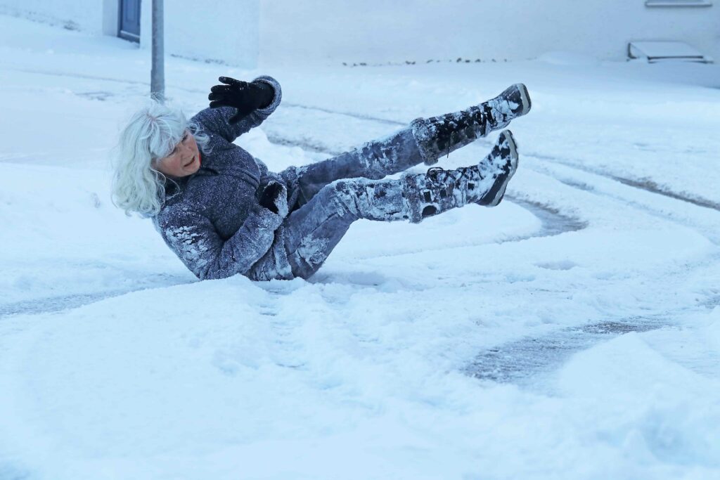 Elderly woman slipping and falling on icy sidewalk during snowy winter conditions.
